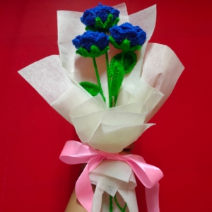 Customizable blue crochet rose bouquet with white wrapping and pink ribbon.