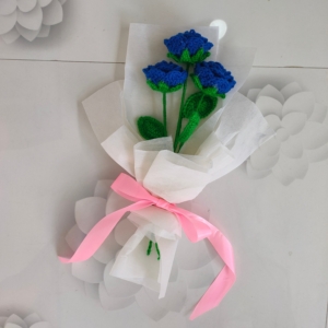 Customizable blue crochet rose bouquet with white wrapping and pink ribbon.