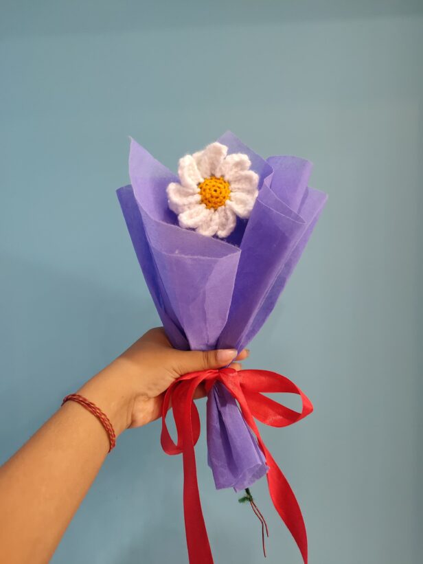 Handmade crochet daisy bouquet wrapped in purple paper with a red ribbon.