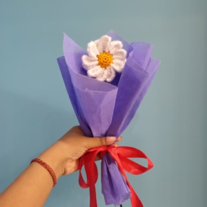 Handmade crochet daisy bouquet wrapped in purple paper with a red ribbon.